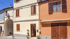 A two-story building with wooden shutters, a stone-paved courtyard, and a large wooden door.