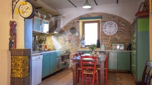 A kitchen with a stone arch, a dining table with chairs, and a clock on the wall.