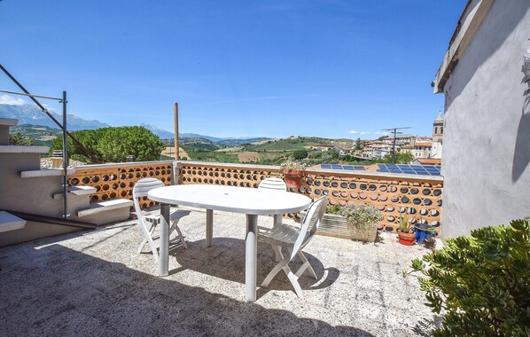 Una terraza con una mesa redonda y sillas, vistas al campo y un edificio con paneles solares.