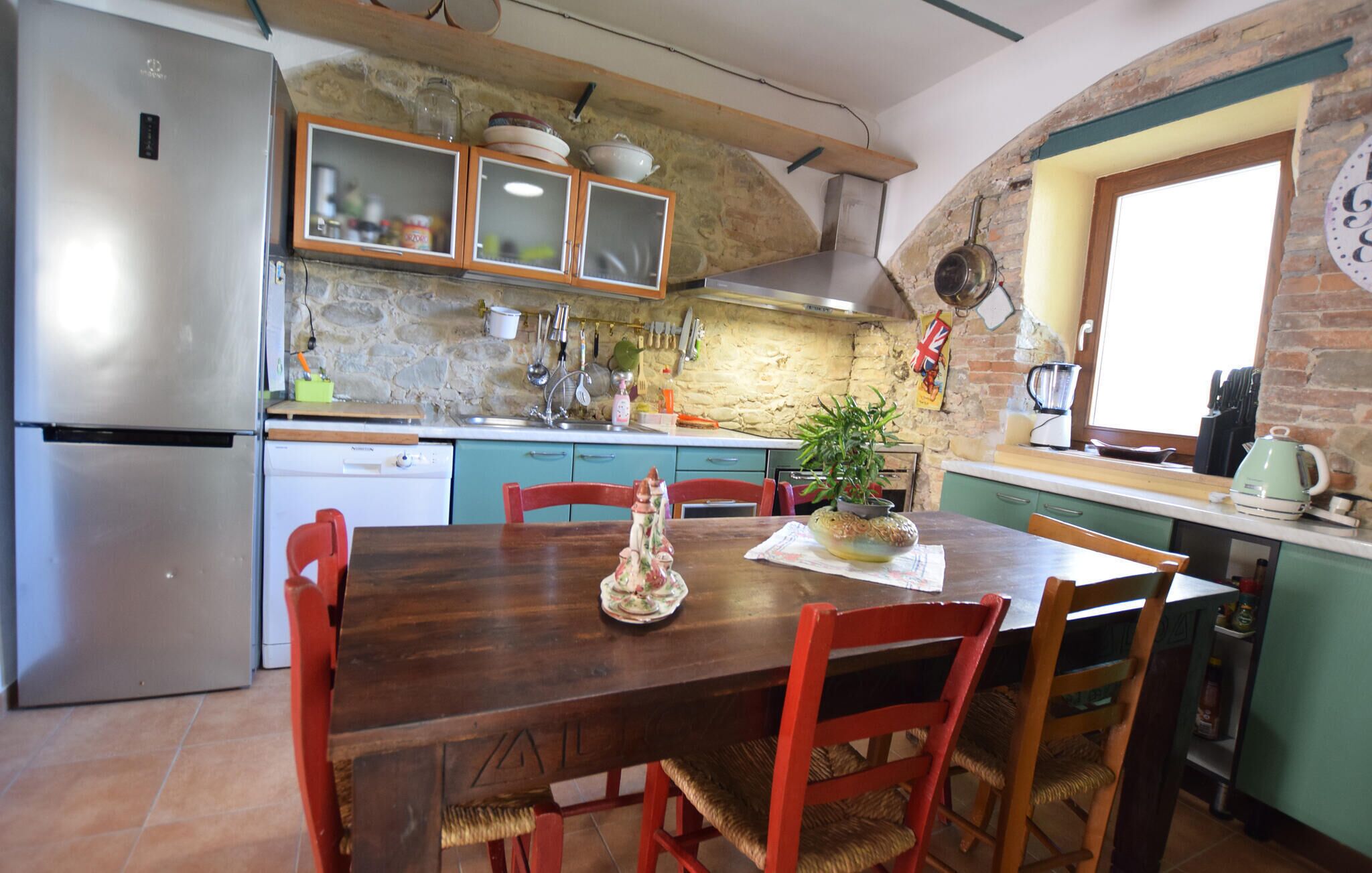 A kitchen with a wooden dining table, chairs, a refrigerator, and a stone wall.