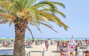 Una playa con palmeras, sillas de playa, sombrillas y una construcción que parece un castillo.