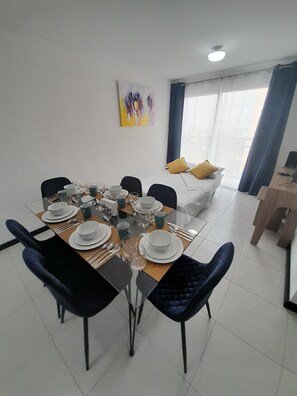 Un comedor con una mesa de vidrio dispuesta para seis personas, rodeado de sillas azul oscuro.
