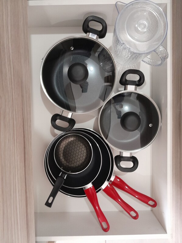 A kitchen drawer containing various cookware including pots, pans, and a strainer.