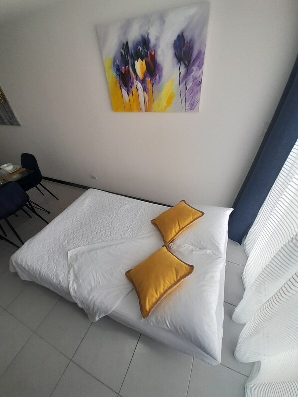 A hotel room with a bed, two pillows, a painting on the wall, a chair, and a window with curtains.