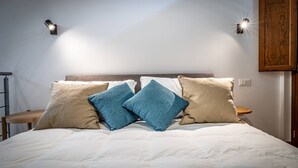 A neatly made bed with a white duvet and two pillows, one blue and one beige, in a room with a wooden headboard and a wall-mounted light fixture.
