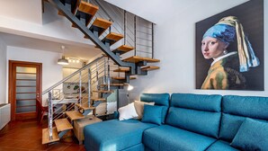A modern living room with a blue sofa, a staircase with wooden steps, and a large painting on the wall.