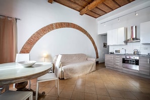 A kitchen with a built-in oven, a microwave, and a stove. There is a round table with a bowl on it and a chair.
