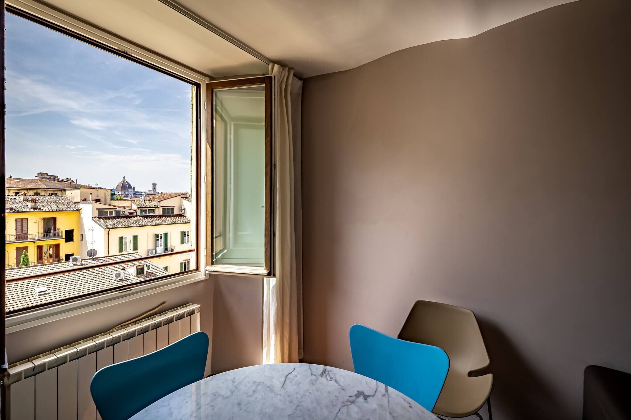 A room with a view of a cityscape, a window, a radiator, and two chairs.