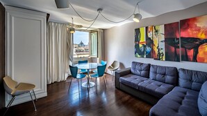 A modern living room with a gray sofa, a dining table with blue chairs, and a view of a cityscape through large windows.