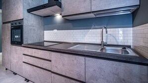 Een moderne keuken met een inbouwoven, een RVS spoelbak en grijze kastjes.