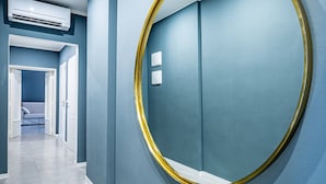 Een gang met een grote ronde spiegel aan de muur, een deur aan het einde en een airconditioningunit in het plafond.