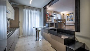 A modern kitchen with a dining area, a bar stool, and a view of the living room.
