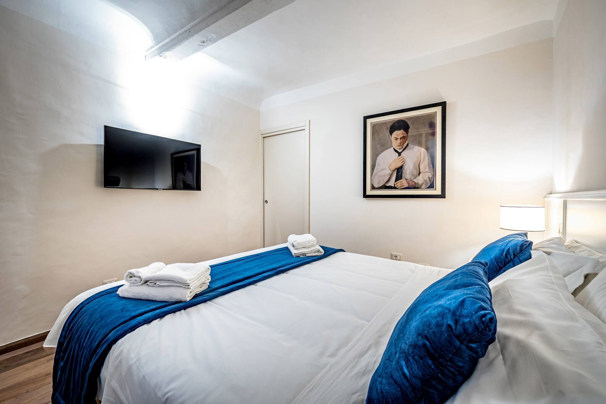 A hotel room with a bed, a flat-screen TV, a framed photo on the wall, and a door.
