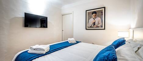 A hotel room with a bed, a flat-screen TV, a framed photo on the wall, and a door.