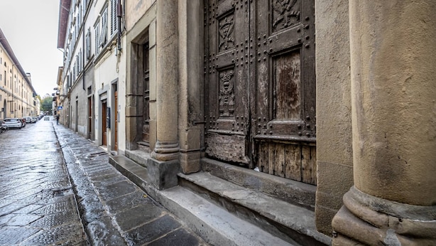 Une rue étroite bordée de bâtiments historiques, une grande porte en bois richement décorée et un chemin pavé de pierres mouillées.