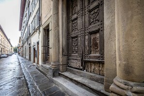 A narrow street with historic buildings, a large ornate wooden door, and a wet cobblestone path. - YiD La Cantoria Luxury Apartment (Firenze)