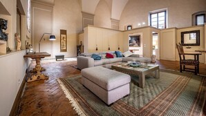 Un salon spacieux avec de hauts plafonds, un grand canapé, une table basse et un tapis à motifs.