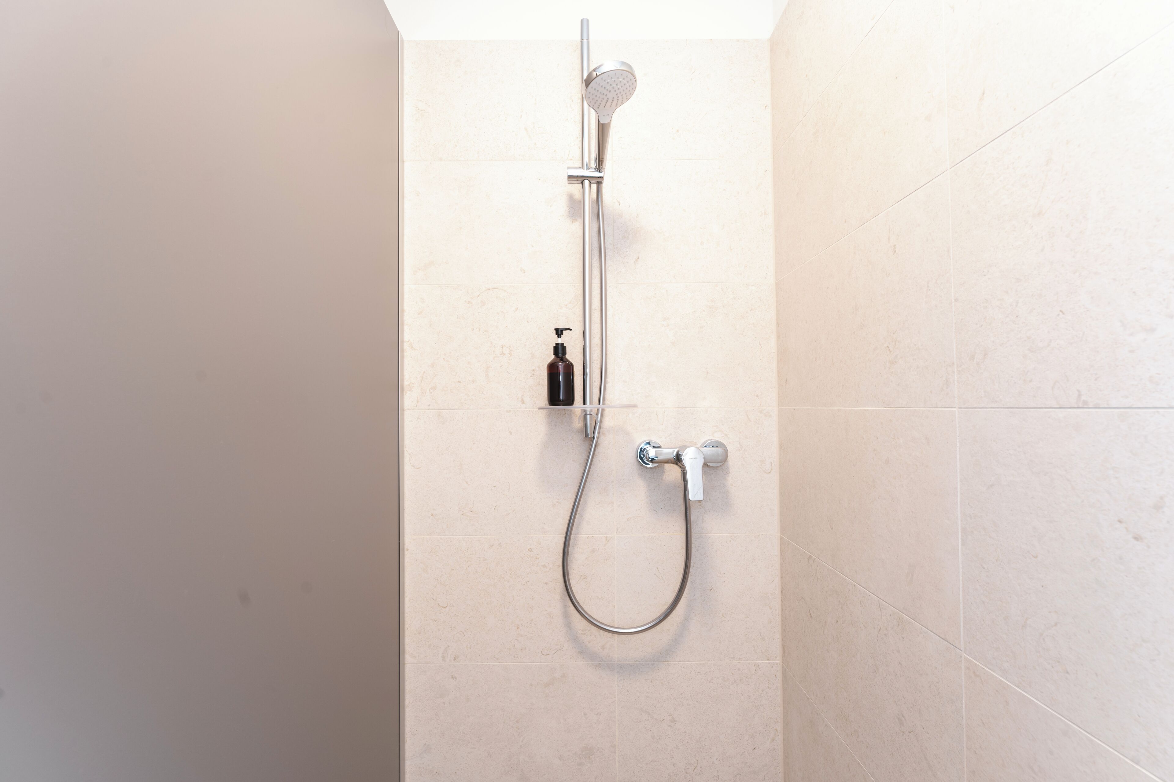 A shower with a handheld showerhead and a wall-mounted faucet.