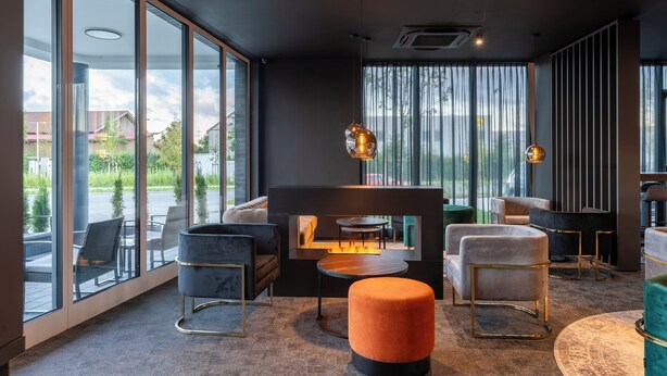 A modern interior with large windows, a fireplace, and contemporary furniture. - JustStay München Hotel & Apartments (Vaterstetten)