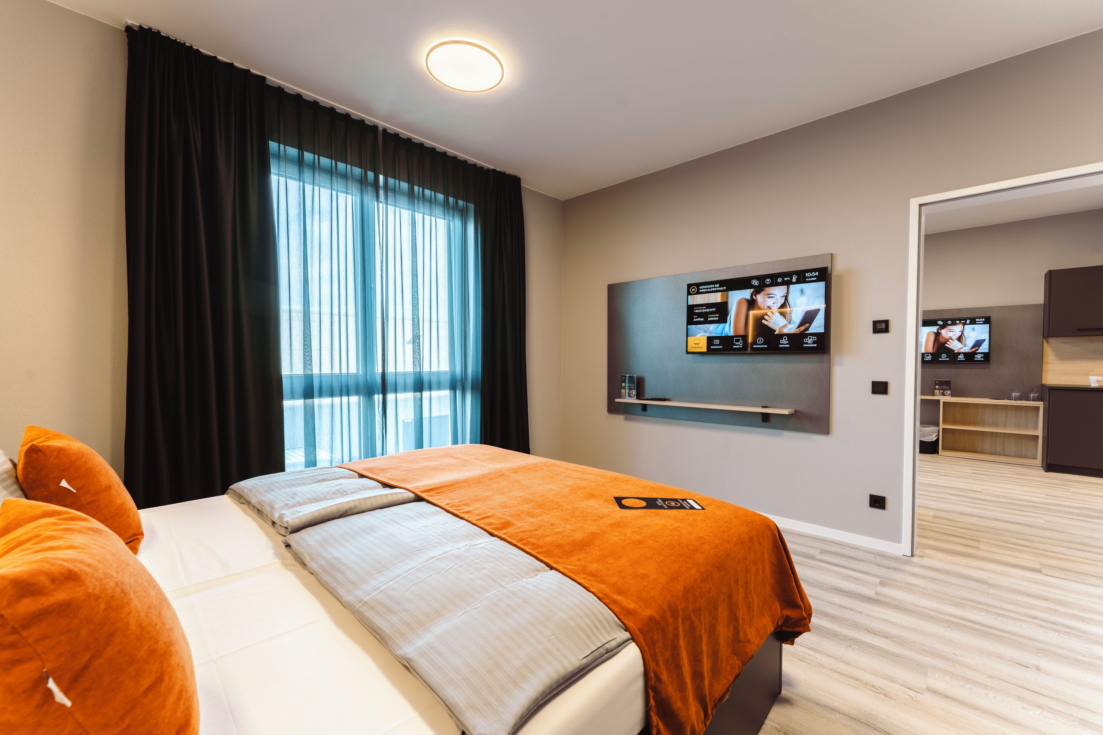 A modern hotel room with a bed, a TV, and a view of the outside.
