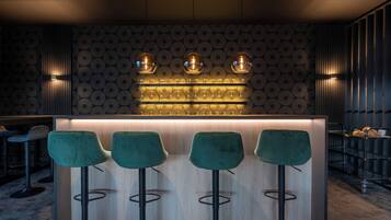 A bar area with three green bar stools, a light wood bar counter, and a patterned wall.