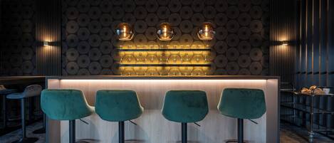 A bar area with three green bar stools, a light wood bar counter, and a patterned wall.