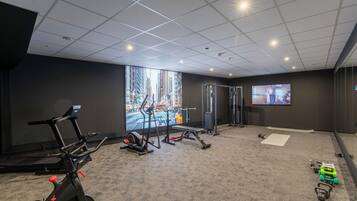 Un gimnasio con equipo de ejercicio, una cinta de correr y una pantalla de televisión.
