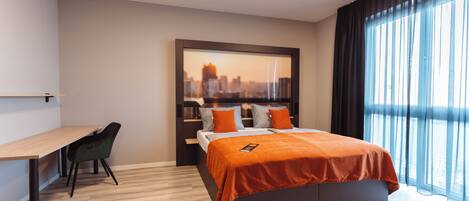 A modern hotel room with a bed, a desk, and a chair.