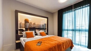 A modern hotel room with a large bed, a cityscape view through a window, and a city skyline reflected in a mirror. - JustStay München Hotel & Apartments (Vaterstetten)