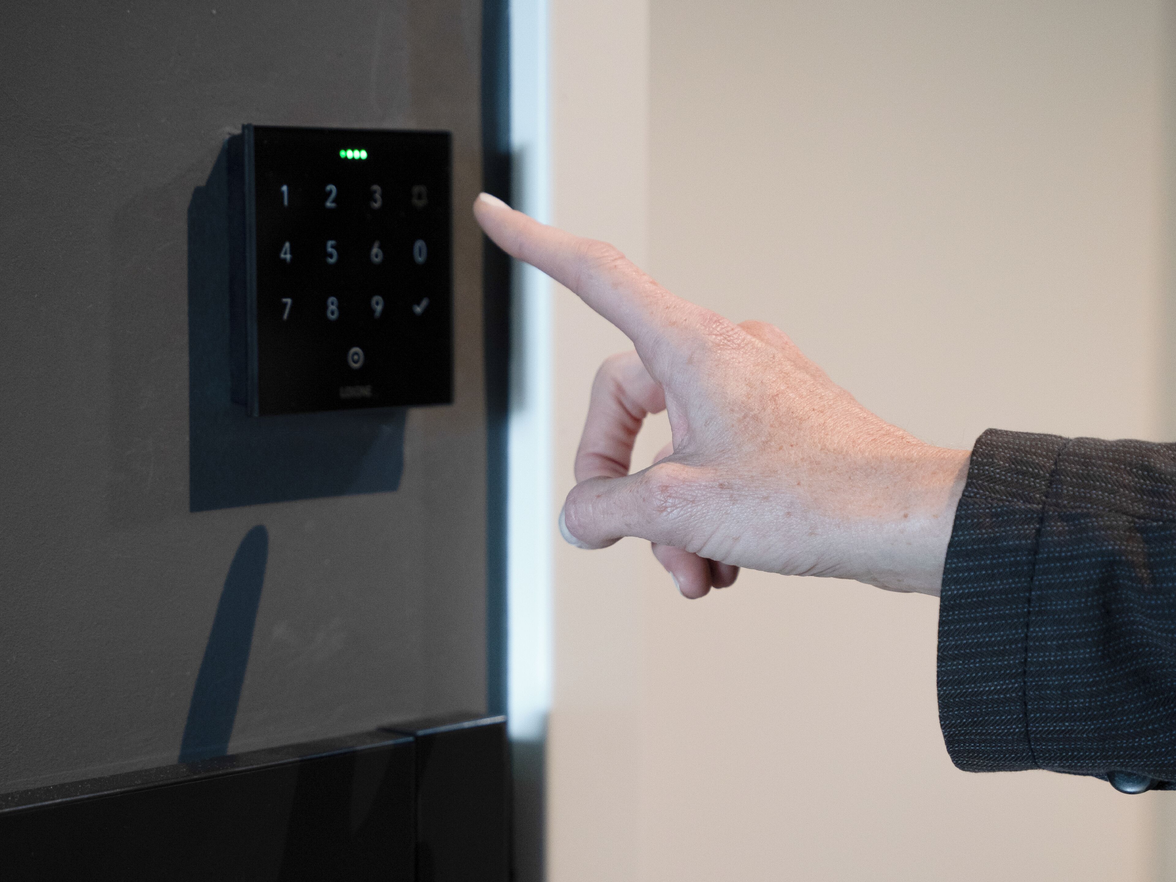 A hand pointing at a digital keypad on a door.