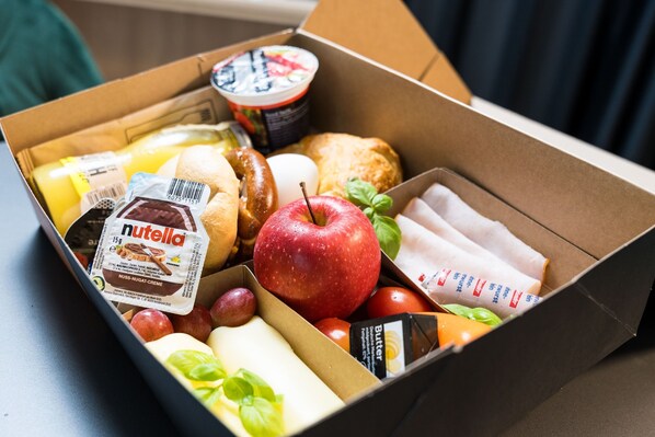 A box of assorted food items including a Nutella bar, apples, and a container of yogurt. - JustStay München Hotel & Apartments (Vaterstetten)