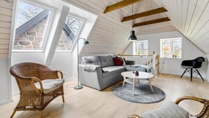 A loft-style room with a sloped ceiling, large windows, a grey sofa, wicker chairs, and a round table. - 2 bedroom beautiful apartment in Kolind (Kolind)