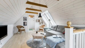 A spacious loft bedroom with a large window, wooden ceiling beams, a grey sofa, a round coffee table, and a television. - 2 bedroom beautiful apartment in Kolind (Kolind)