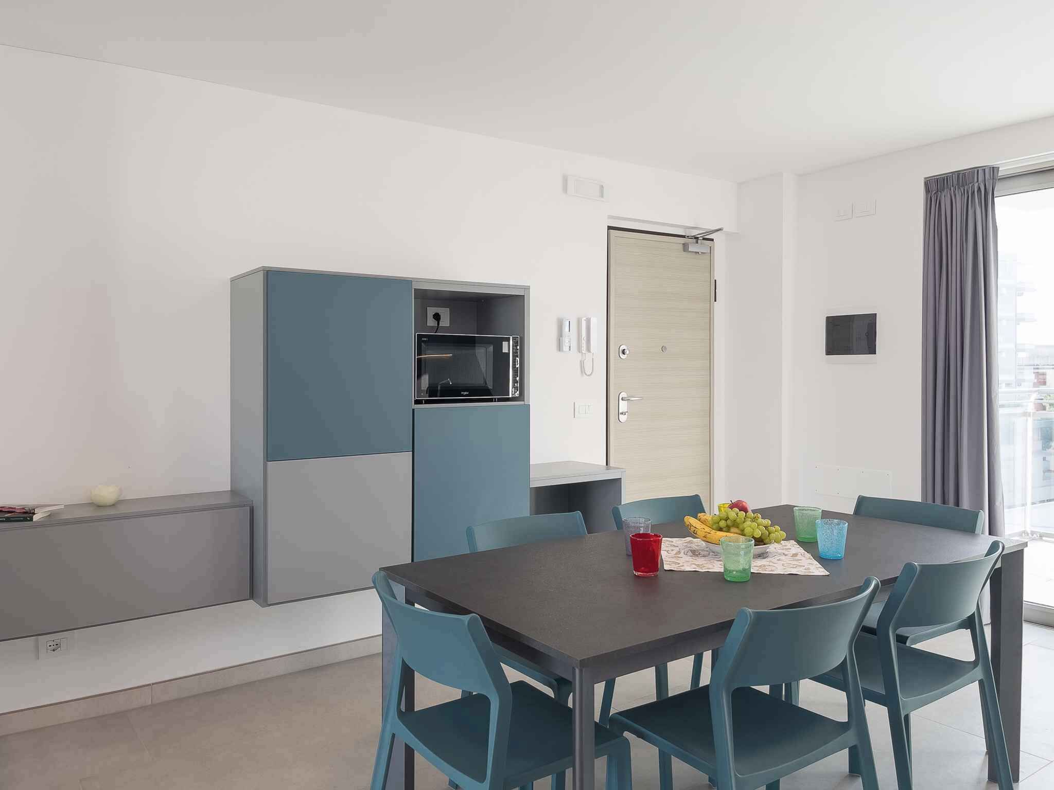 Een moderne eethoek met een tafel voor vier personen, een magnetron en een koelkast op de achtergrond.