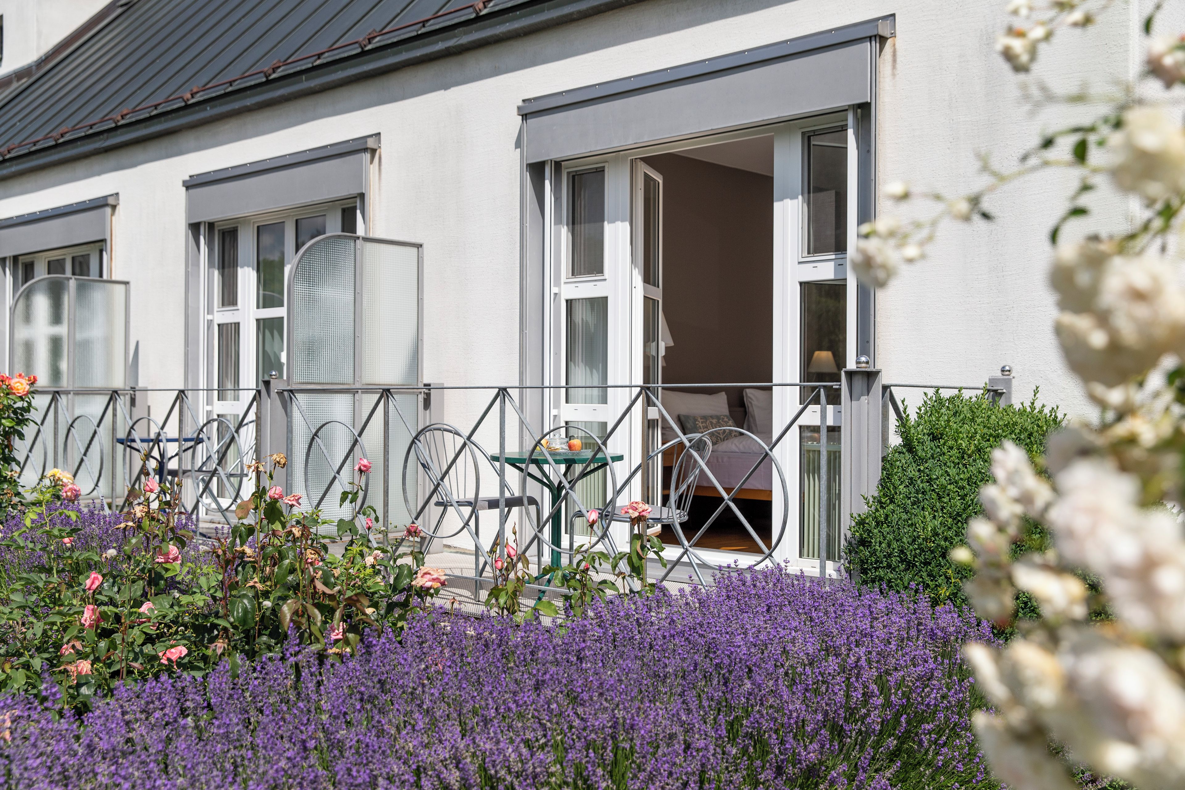 Un bâtiment doté d’un balcon, d’une table et de chaises, entouré de fleurs violettes.