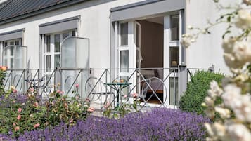 Un bâtiment doté d’un balcon, d’une table et de chaises, entouré de fleurs violettes.