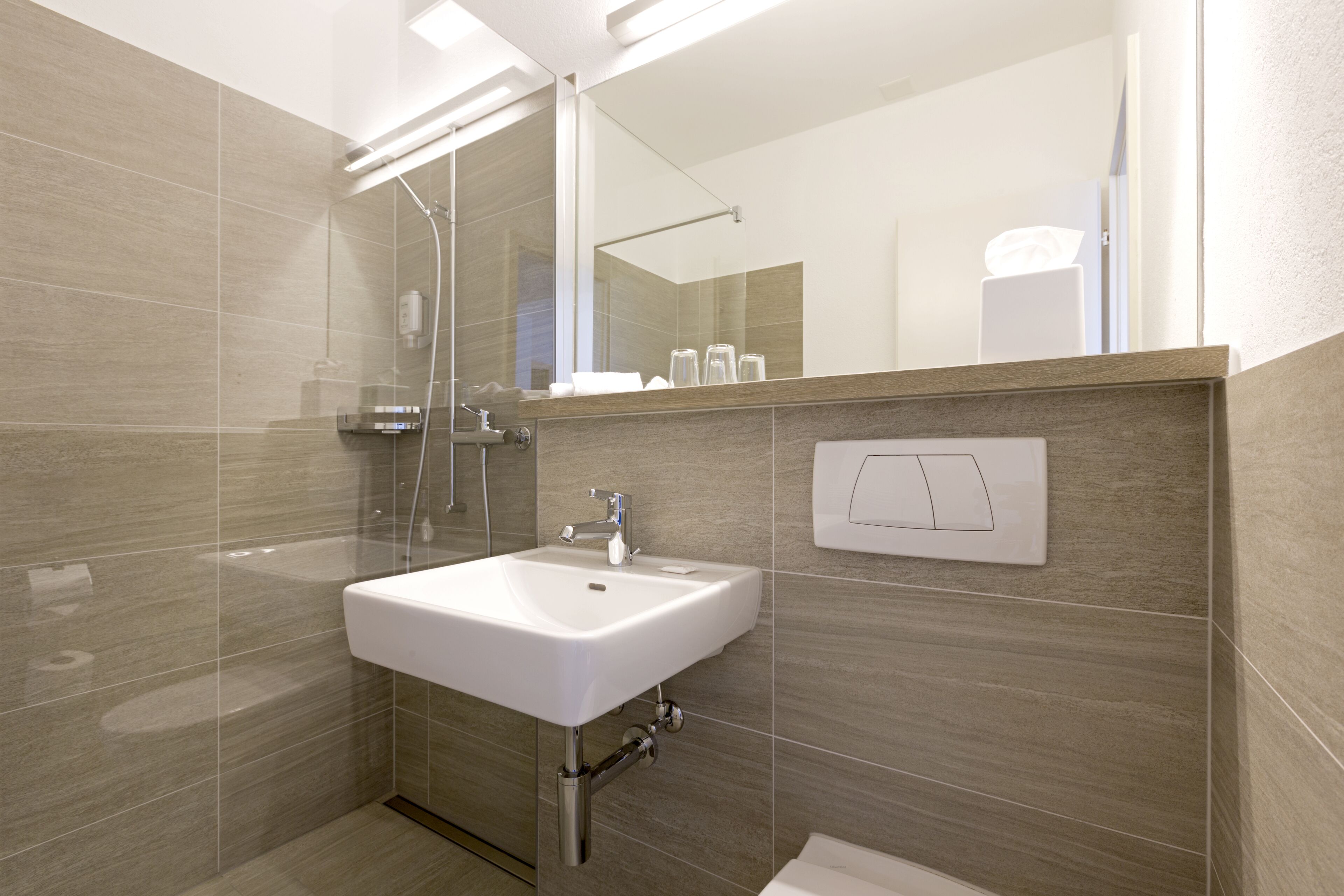 Un baño moderno con un lavamanos blanco, cabina de ducha con mampara de vidrio y un espejo sobre el lavamanos.