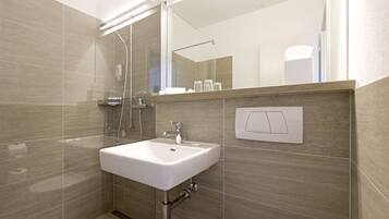 Un baño moderno con un lavamanos blanco, cabina de ducha con mampara de vidrio y un espejo sobre el lavamanos.