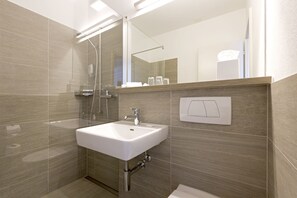 A modern bathroom with a white sink, a glass shower enclosure, and a mirror above the sink. - See & Park Hotel Feldbach (Steckborn)