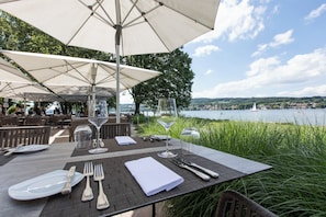An outdoor dining area with tables set for two, overlooking a body of water. - See & Park Hotel Feldbach (Steckborn)
