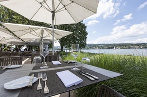 Un área de comedor al aire libre con mesas preparadas para dos, con vista a un cuerpo de agua.