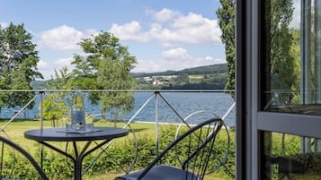 Una terraza con mesa y sillas que da a un lago, con árboles y colinas al fondo.