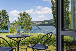 A terrace with a table and chairs overlooking a lake, with trees and hills in the background. - See & Park Hotel Feldbach (Steckborn)