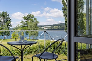 Una terraza con mesa y sillas que da a un lago, con árboles y colinas al fondo.