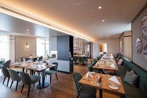 A modern dining area with multiple tables and chairs, a long counter, and a seating area with a sofa. - See & Park Hotel Feldbach (Steckborn)