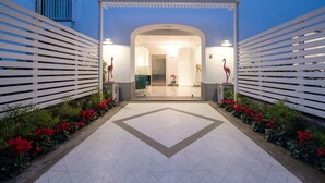 A hotel entrance with a tiled pathway leading to an arched doorway, flanked by white slatted fences and red flamingo statues. - Suite Agave close to the centre of Sorrento (Sant´Agnello)