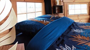 A wooden cabin bedroom with a bed, two windows, and a wooden ceiling.