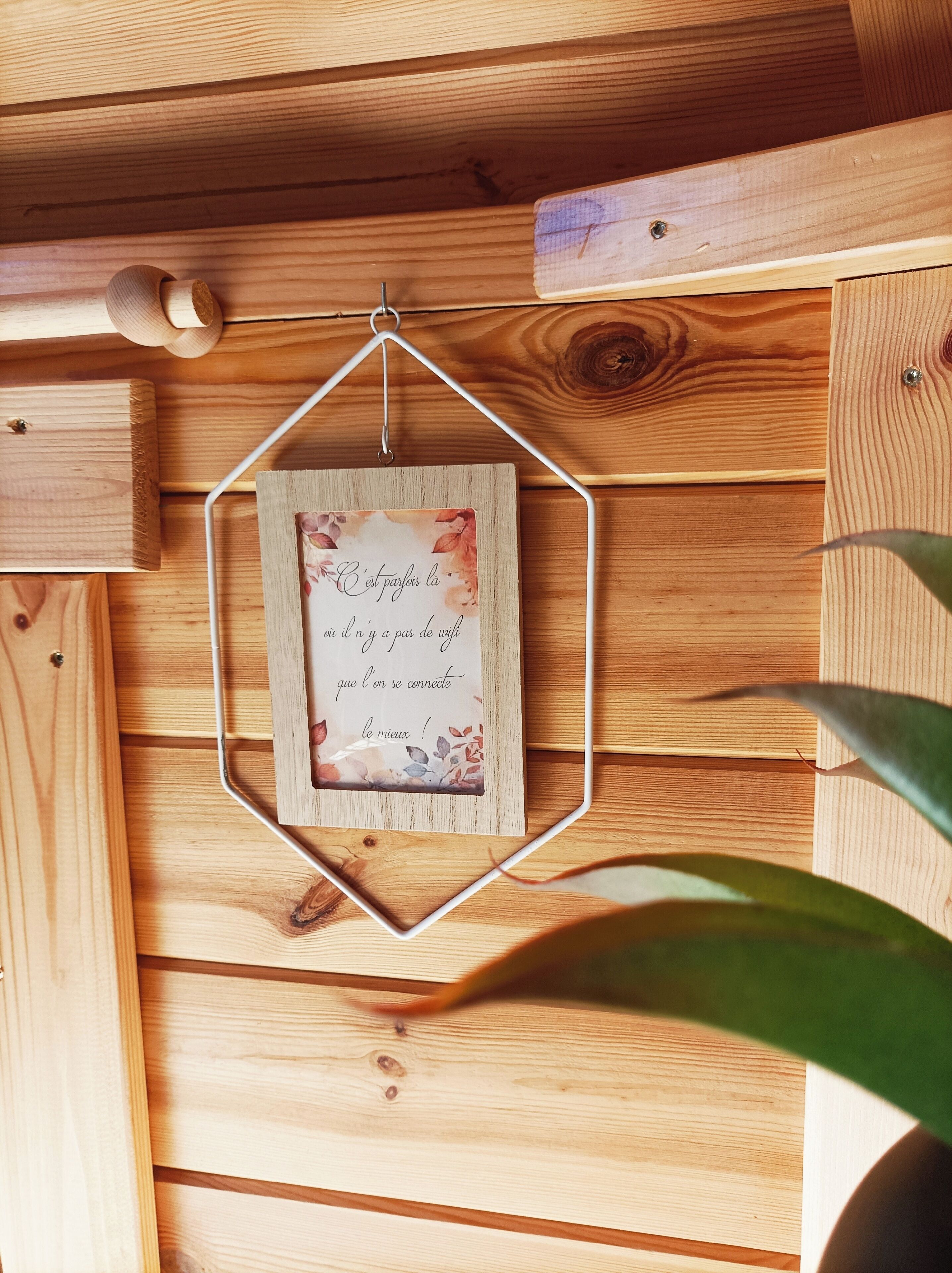 A hexagonal wooden frame with a printed quote hanging on a wooden wall.
