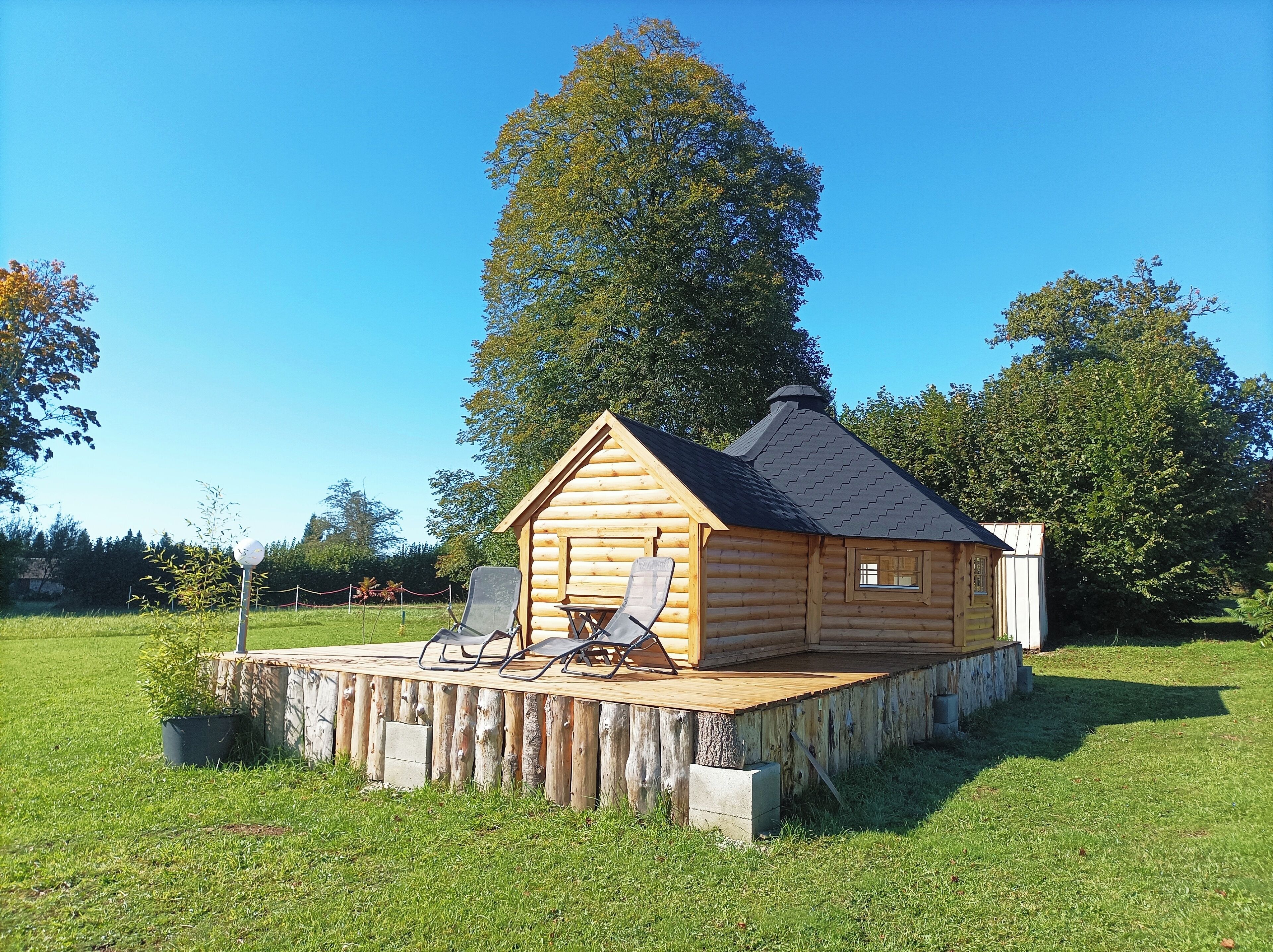 A wooden cabin with a deck, two chairs, and a small window.