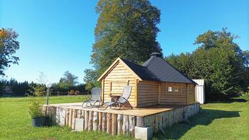 A wooden cabin with a deck, two chairs, and a small window.